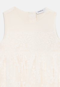 Robe en dentelle crème avec un corsage texturé, un motif floral et une jupe froncée. Présente un col rond et une fermeture en goutte d'eau au dos.