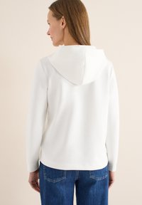 Sweat à capuche blanc avec une grande capuche douce, des manches longues et une texture lisse, associé à un jean bleu présentant un design classique à cinq poches.