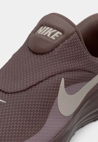 Παπούτσι Nike slip-on σε απαλή μωβ απόχρωση με υφασμάτινο επάνω μέρος, διακοσμημένο με στρογγυλό λογότυπο και ανοιχτό γκρι λογότυπο Swoosh στο πλάι.