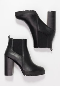 Pár černých kožených kotníkových bot s elastickými bočními panely a blokovými podpatky na bílém pozadí.