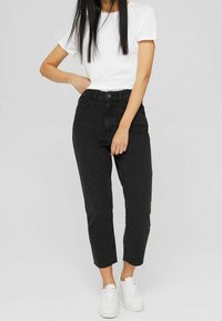 Vaqueros negros de corte alto con un fit recto, que cuentan con un bajo sin terminar y cinco bolsillos, combinados con una camiseta blanca de manga corta básica y zapatillas blancas.