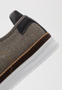 Sneaker in tessuto grigio con accenti marroni e beige, dotato di un cappuccio per il tallone in pelle e una suola in gomma bianca. Dettagli cuciti visibili.