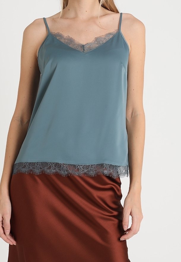 Camisole en satin turquoise avec bordure en dentelle au niveau du décolleté et de l'ourlet, dotée de bretelles spaghetti ajustables, portée sur une jupe en satin marron.