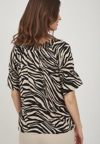 Blusa animalier in beige e nero, caratterizzata da una vestibilità comoda, maniche corte e un colletto arricciato. Texture morbida con design fluido.