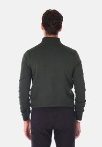 Polo a maniche lunghe verde scuro con colletto, design aderente e polsini a coste, abbinato a jeans scuri. Tessuto morbido, dettagli minimi.