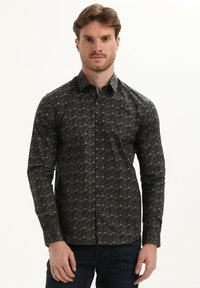 Camisa de manga larga en tela oscura con un patrón que presenta diseños geométricos en tonos de gris y marrón, con un cuello clásico y cierre de botones en la parte delantera.