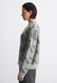 Pulover gri deschis cu un model tricotat texturat, având un decolteu rotund cu margini ondulate și mâneci largi. Material moale cu un aspect confortabil și cald.