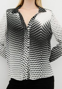 Black and white blouse with a gradient polka dot pattern. Features a button-down front, collar, and long sleeves. Lightweight, smooth fabric.