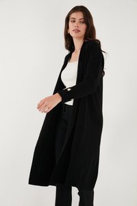 Svart ribbad cardigan med långa ärmar, öppen front och en avslappnad passform. Har guldknappdetaljer på ärmsluten. Mjuk textur.