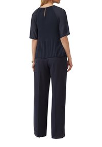 Blouse plissée marine à manches courtes et détail en forme de trou de serrure à l'arrière, associée à un pantalon marine ample, le tout en tissu lisse.