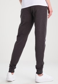 Antracietgrijze joggingbroek van zachte stof, met taps toelopend ontwerp, elastische tailleband en omgeslagen enkels. Draagt witte sneakers.