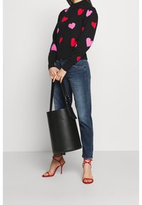 Suéter negro con patrones de corazones multicolores, combinado con unos jeans de mezclilla azul claro. Bolso tipo cubo negro y sandalias de tacón alto rojas con tiras.
