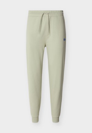 Pantaloni jogger beige chiaro con vita elastica, coulisse, polsini a coste e piccolo patch con logo blu sulla coscia destra.