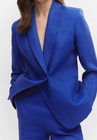 Blazer en lin bleu royal avec un col à revers cranté, une fermeture à un bouton et des poches devant, présentant une coupe décontractée et des détails de couture précis.