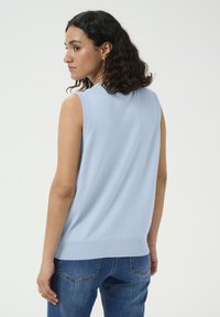 Top en tricot sans manches de couleur bleu clair avec un col rond, un ourlet côtelé et une texture lisse, associé à un jean bleu.