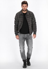 Graue Karojacke mit schwarzen Akzenten, kombiniert mit einem schwarzen Hemd und grauen Jeans. Schwarze Schnürstiefel vervollständigen das Outfit.