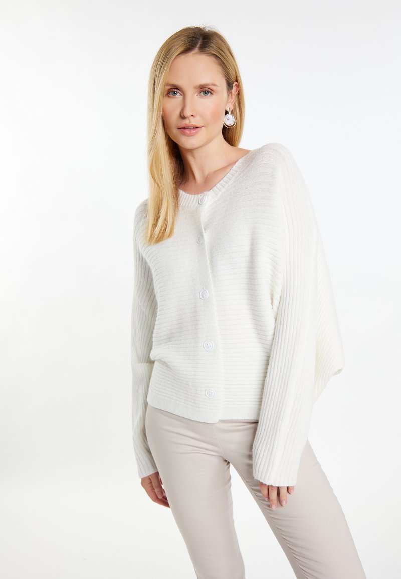 Witte geribbelde cardigan met een relaxed fit, voorzien van een ronde halslijn, knoopsluiting en lange mouwen, gecombineerd met lichtbeige broeken.