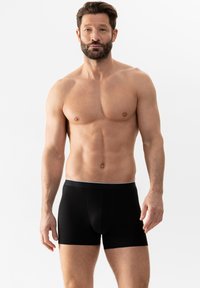Boxer-briefs noirs avec une ceinture élastique douce. Le tissu semble extensible et lisse, s'ajustant bien au corps. Pas de motifs ni d'ornements visibles.