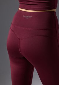 Maroon active leggings with fitted design, smooth texture, and visible stitching detail, featuring a logo at the waistband.