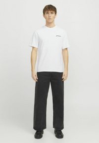 Camiseta de algodón blanca con mangas cortas y cuello redondo, combinada con pantalones vaqueros de pierna ancha negros y calzado negro. Diseño simple con detalles mínimos.