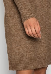 Brun stickad klänning med ribbade muddar och fåll, med en mjuk textur och en avslappnad passform, som framhäver en enda handgest.