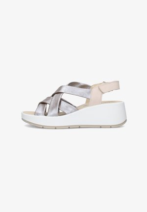 Sandalo con zeppa con cinturini incrociati in argento metallizzato, cinturino beige al tallone con velcro e suola bianca spessa, vista laterale.