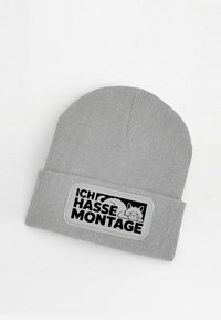 Gray knit beanie with a folded brim, featuring a black patch with the text "ICH HASSE MONTAGE" and a cartoon cat illustration.