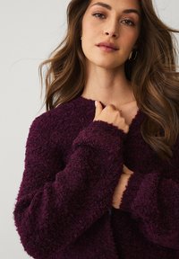 Pluizige, dieppaars cardigan met een ronde hals en lange mouwen. Zachte textuur, zichtbare stiknaden en een ontspannen pasvorm.