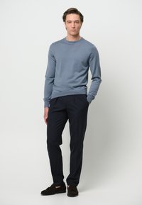 Helles blaues Sweatshirt, dunkle marineblaue Hose und braune Wildlederschuhe. Taillierte Passform mit langen Ärmeln und gerippten Bündchen. Schlichte, klare Linien.