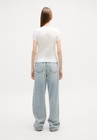 Camiseta blanca de manga corta combinada con vaqueros de pierna ancha de color azul claro. La tela parece suave con un acabado ligeramente texturizado.