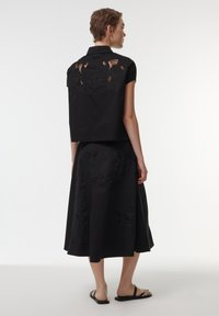 Black cropped shirt with short sleeves, featuring intricate cut-out floral design on the back, paired with a flowing black skirt.