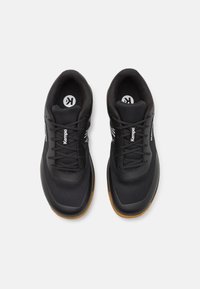 Black athletic shoes with mesh fabric upper, overlapping panels, and lace-up design. Features gum rubber outsole and white branding accents.