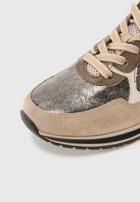 Primo piano di una scarpa da ginnastica beige e argentata, con lacci beige, tessuto a rete e una suola in gomma nera e beige.