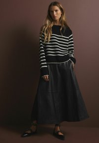 Gestreifter Pullover in Schwarz und Weiß mit langen Ärmeln, kombiniert mit einem fließenden schwarzen Leder-Maxi-Rock. Verfügt über einen einfachen Ausschnitt und strukturierte Stoff.