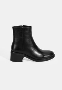 Bottine en cuir noir avec un bout rond et un talon épais, dotée d'une fermeture éclair à l'arrière et d'une texture lisse et brillante.