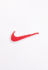 Nike-logotyp i texturerat rött tyg med vit kant, broderad på en enfärgad vit bakgrund, med en böjd, swoosh-form.