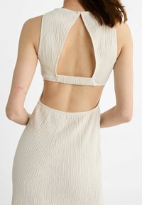 Ensemble beige texturé composé de deux pièces, comprenant un haut court avec une ouverture dans le dos et une jupe moulante, mettant en valeur sa surface côtelée.