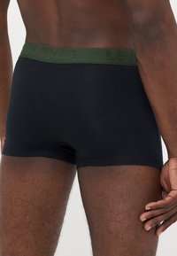 Black cotton boxer shorts with a green textured waistband, featuring the embossed logo "Levis." The fabric appears smooth and fitted.