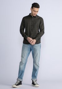 Camisa negra de botones con un patrón amarillo, combinada con jeans de mezclilla azul claro y zapatillas negras de caña alta. Tela suave con mangas largas.