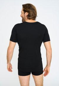 Sort kortærmet skjorte lavet af blødt stof, med rund halsudskæring. Bæres med matchende sorte shorts, der viser en tætsiddende design.