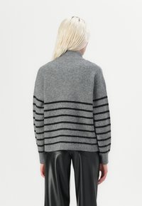 Pull en maille grise avec des rayures horizontales noires, texture côtelée et col montant. Porté avec un pantalon en cuir noir.
