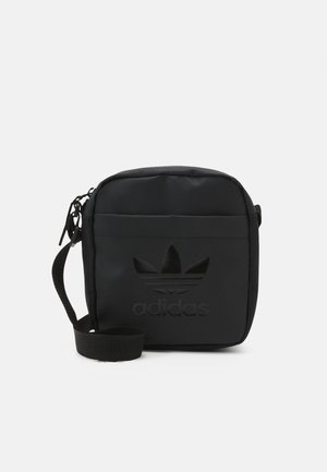 Kleine schwarze Umhängetasche mit verstellbarem Riemen, vorderer Reißverschlusstasche und geprägt geprägtem Adidas-Trefoil-Logo auf einfarbigem Hintergrund.