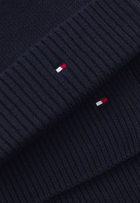 Marineblå strikket sweater med ribbet tekstur. Har små røde, hvide og blå logo-accenter. Stoffet ser blødt og tykt ud.