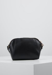 Svart läder kosmetikväska med en texturerad yta, rundad form, blixtlås i guldton och sidrem för att bära.