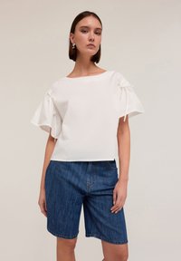 Top bianco a maniche corte con scollatura rotonda e dettagli con fiocco sulle maniche, abbinato a pantaloni shorts in denim blu medio. Tessuto morbido.