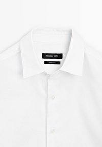 White button-up shirt with a classic collar, made of textured fabric, featuring subtle branding on a black label inside the collar.