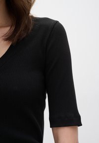 Svart ribbad kortärmad topp med V-ringning, slät textur och figurnära design, som framhäver tygets stretch och komfort.