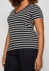 T-shirt a maniche corte con scollo a V a righe orizzontali blu navy e crema. Materiale in morbido cotone con una vestibilità comoda. Piccolo dettaglio logo sul petto.