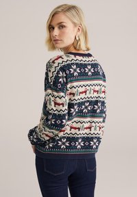 Pletený svetr s krémovým základem a slavnostním vzorem s modrými, zelenými a červenými soby, sněhovými vločkami a vánočními stromy. Žebrované manžety a lem.