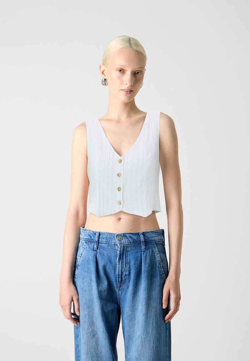 White sleeveless crop top with vertical pinstripes, v-neck, and five round buttons in front; worn with loose blue denim high-waisted pants.